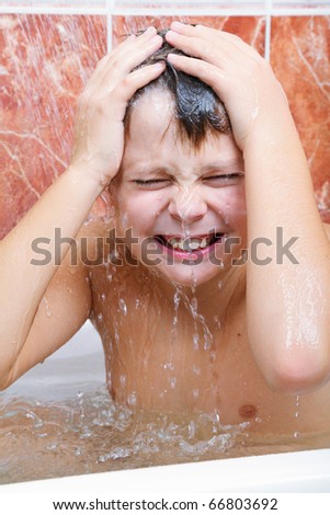 Squinting boy in bath under water spurts flushing from shower
