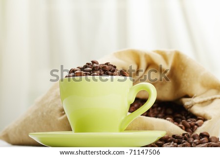 Green cup with coffee beans against textile bag
