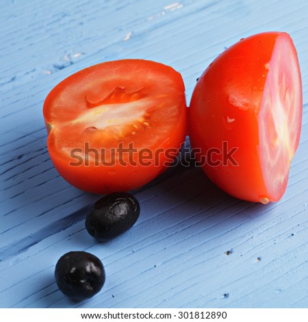 Ripe cut tomato and black olives over blue wooden tabletop