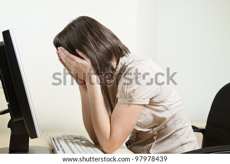 Woman covering face with hands while sitting at computer in office