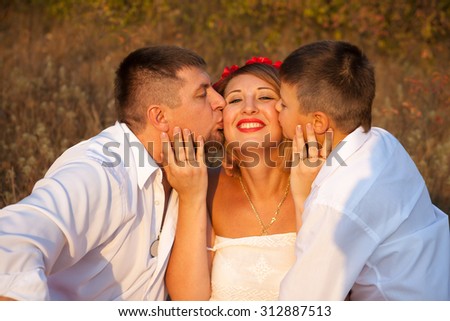 Dad and son kissing his mother on the cheek on both sides, in the park