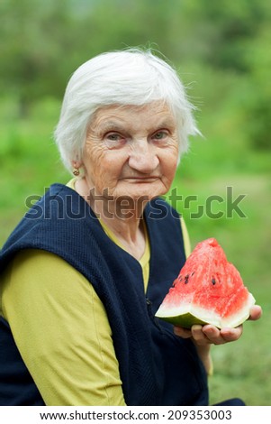 Elderly happy woman eating watermelon in the garden