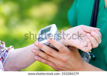 Male doctor checking senior woman blood pressure