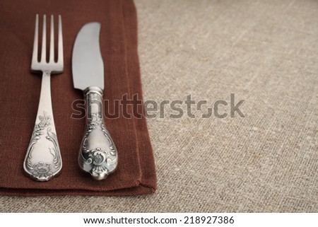 Table setting. Vintage fork and knife on brown napkin with linen tablecloth and copyspace.