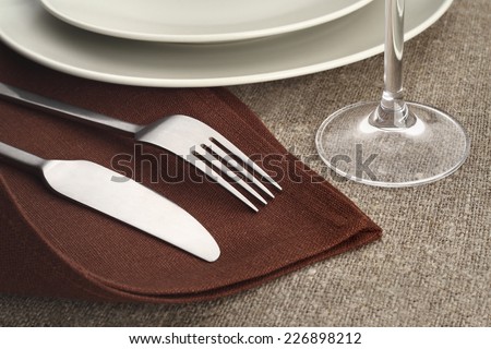 Table setting. Cutlery set with fork, knife, plate and glass on brown linen napkins and tablecloth.