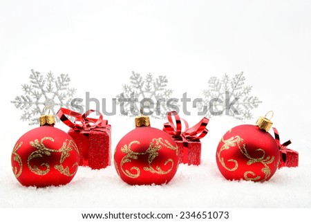 Decoration of red christmas gifts and baubles and snowflakes on snow on white background