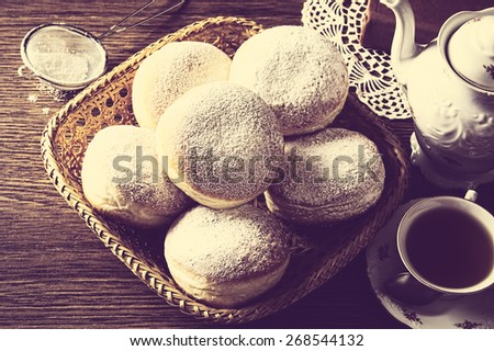 Studio shot of donuts in wicker basket view from above with cup of tea,coffee with kettle and book on napkin in vintage effect
