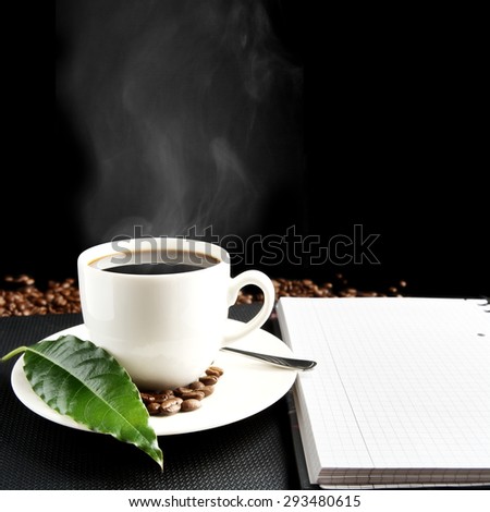 Cup of black coffee with mist with notebook, green coffee leaf, coffee beans at breakfast on black background
