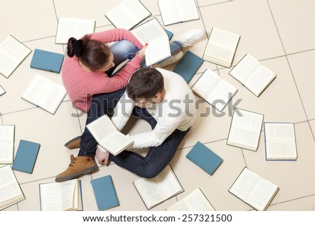 Young woman and man reading a book, top view. Blurred text is unreadable
