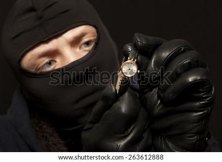 Thief. Man in black mask with a golden watch. Focus on golden watch