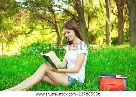 Portrait of beautiful young girl reading a book in the park at summer