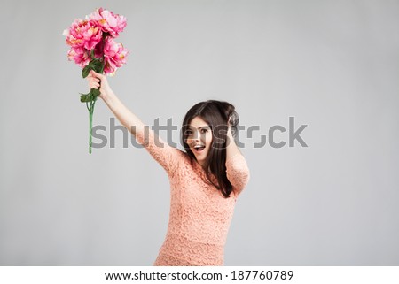 Exciting young woman smiling and holding flowers, over grey background