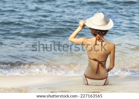 Beautiful back side of model in bikini and hat sitting down.