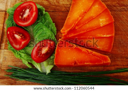 orange aged delicious cheddar cheese chop with slice on wooden plate with tomatoes , chives and salad . isolated over white background