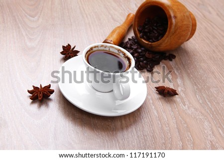 sweet hot drink : black Turkish coffee in small white mug with mortar and pestle , coffee beans over a wooden table , decorated with cinnamon sticks and anise stars