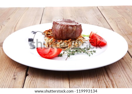 grilled beef fillet medallions on noodles with tomatoes and thyme twigs on white plate over wood