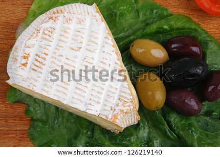 brie cheese on wooden platter with olives and tomato isolated over white background