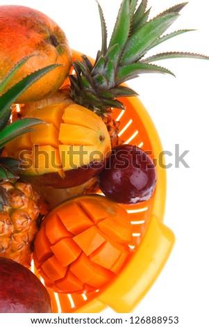 diet food - a lot of fresh raw tropical fruits include pineapple red plum and green mango in orange colander isolated over white background