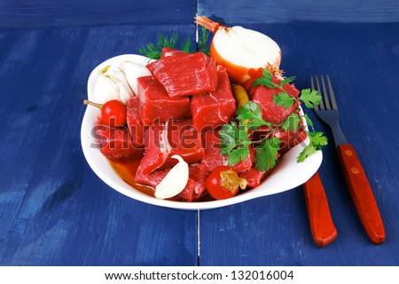 uncooked fresh beef meat chunks on white bowls with vegetables and red peppers serving on blue table with cutlery