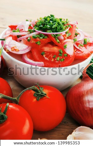 healthy food : fresh tomato salad in white bowl with bunch of chives and raw tomatoes on twig , onion, and garlic over wooden table