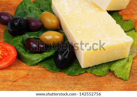 gold swiss cheese on wooden platter with olives and tomato isolated over white background