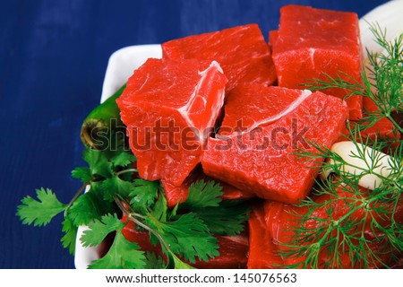 raw fresh beef meat slices in a white bowls with dill and green hot peppers serving over blue wooden table