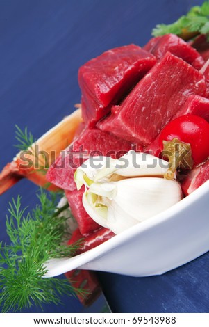 slices of raw fresh beef meat fillet in a white bowls with garlic and red peppers serving on blue table with cutlery