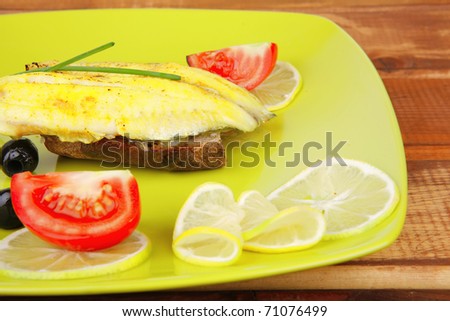 roast fish fillet with tomatoes,chives and bread on plate over wood