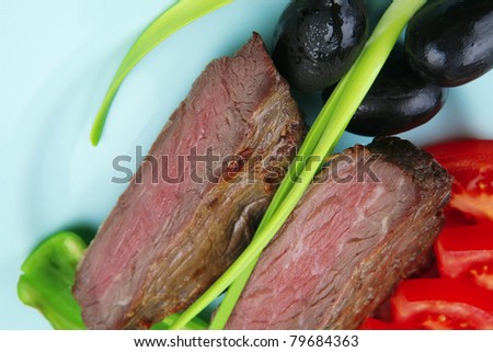 meat food : roasted fillet mignon on blue plate with pepper tomatoes and black greek olives over blue wooden table