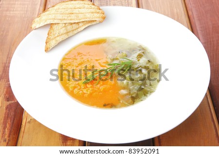 european cuisine: vegetable soup with toasts on white dish over wooden table