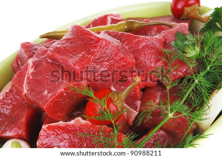 slices of raw fresh beef meat fillet in a ceramic dish with garlic and red peppers isolated over white background
