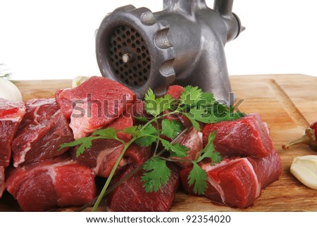 uncooked fresh beef meat chunks on wooden cutting plate with green hot and red peppers and grinder isolated over white background
