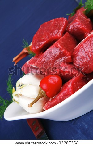 raw fresh beef meat slices in a white bowls with onion and red peppers serving on blue table with cutlery