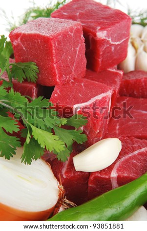 uncooked fresh beef meat chunks on ceramic bowls with vegetables and greenery isolated over white background