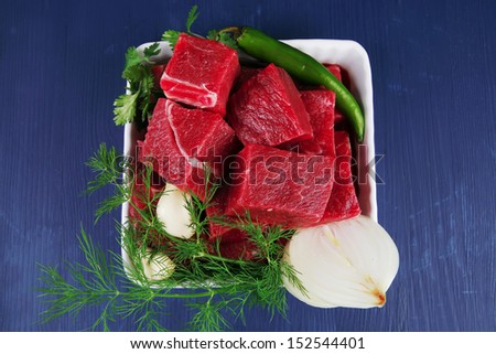 slices of raw fresh beef meat fillet in a white bowls with dill and green peppers serving over blue wooden table