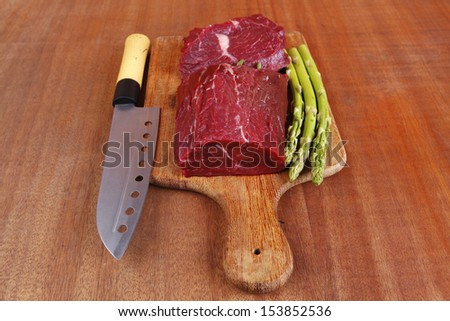 red fresh raw beef veal fillet with asparagus and stainless steel chef knife on cutting plate over wooden table prepared to use