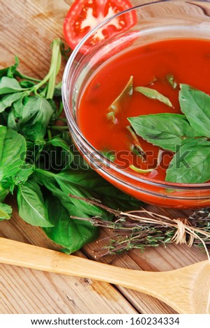 natural vegetable diet food : hot tomato soup with basil thyme and raw tomatoes in transparent bowl over red mat on wood table ready to eat