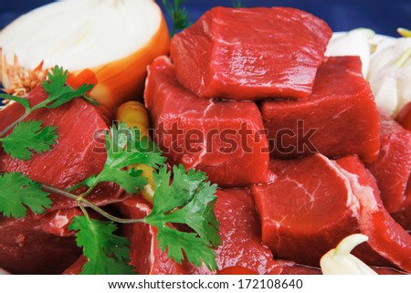 raw fresh beef meat slices in a white bowls with onion and red peppers serving on blue table with cutlery