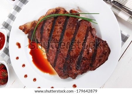 fresh rich juicy grilled beef meat steak fillet with marks on white plate over wooden table decorated with sauces and cutlery new york style