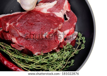 raw beef meat with thyme and pepper on black ceramic pan isolated on white background