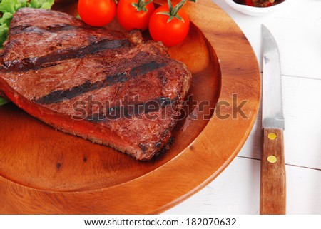 lunch of fresh rich juicy grilled beef meat steak fillet with marks on wooden plate over white table served with vegetable salad and cutlery, new york styled cuisine