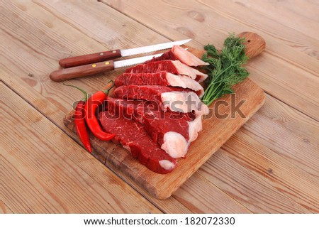fresh raw beef meat steak\'s on wooden cut board over wooden table with dill and stainless steel knife