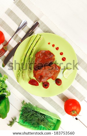 roast stew beef pork meat served with vegetables on green plate and cutlery on napkin over wooden table with red hot peppers