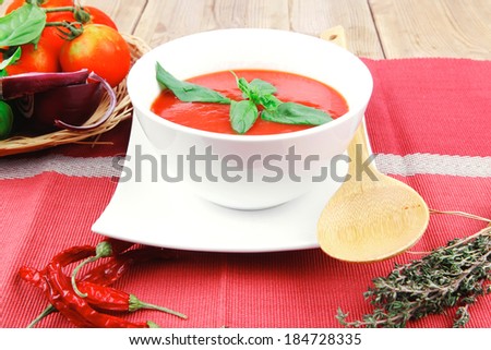diet food : hot tomato soup with basil thyme and dry pepper in big bowl over red mat on wood table ready to eat