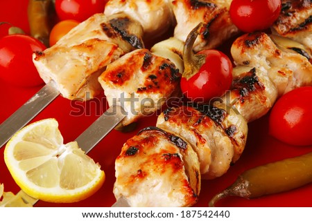 fresh grilled chicken shish kebab served wtih tomato cherry hot peppers on skewers over red plate isolated on white background