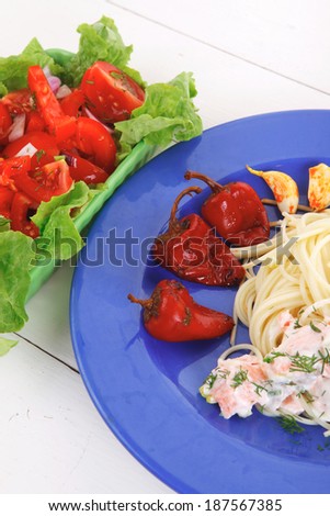 fresh rose wild salmon baked in cream cheese sauce with italian pasta and red hot pepper on blue plate over white wooden table with vegetable salad