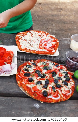 prepare hand made pizza with olives and tomatoes on wooden table on picnic with different kind of cheeses
