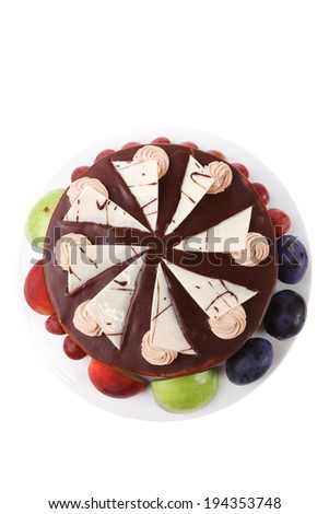 chocolate cream brownie cake topped with white chocolate slice and cream flowers decorated with fruits apple plum and grape on plate isolated over white background