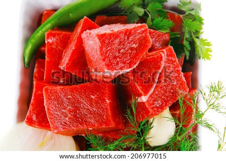 uncooked fresh beef meat chunks on white bowls with green hot peppers and vegetables isolated over white background