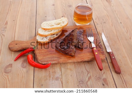 fresh beef meat steak with red hot pepper and bun slices served on plate with whiskey on wood over table with cutlery